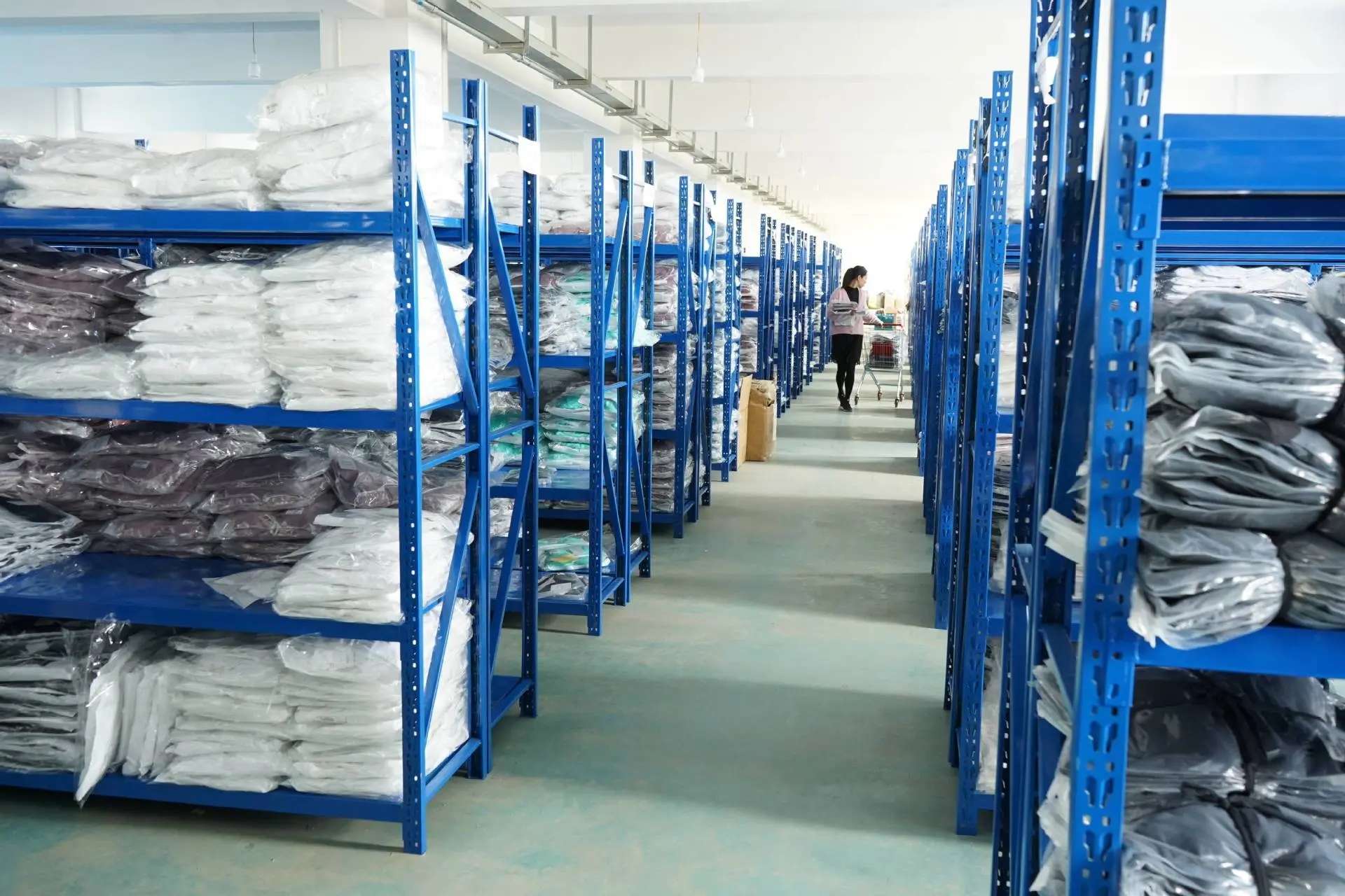 This picture shows a section of Aprilluck's sportswear warehouse, displaying the company's commitment to quality and organization. The space is well-organized and spacious, with rows of shelves and storage containers lining the walls. The lighting is bright and even, ensuring that every item is clearly visible. The color palette is primarily neutral, with shades of white, gray, and black dominating the space. The image is taken from a medium angle, showing the vast expanse of the warehouse and the sheer volume of items it contains. The composition is balanced, with the shelves and containers arranged in a neat and orderly fashion. Overall, this image offers a glimpse into the efficiency and professionalism of Aprilluck's sportswear operations.