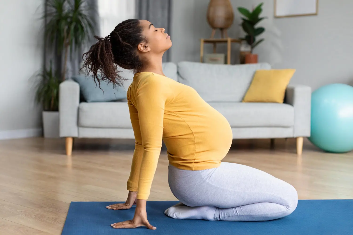 happy-pretty-young-black-pregnant-female-with-big-belly-doing-exercises-practicing-yoga-living-room.